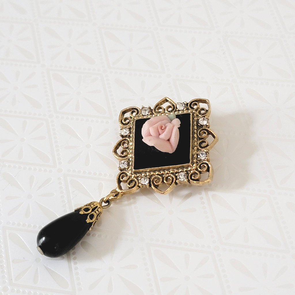 1928 brand black dangle and pink porcelain rose brooch, with gold tone filigree.