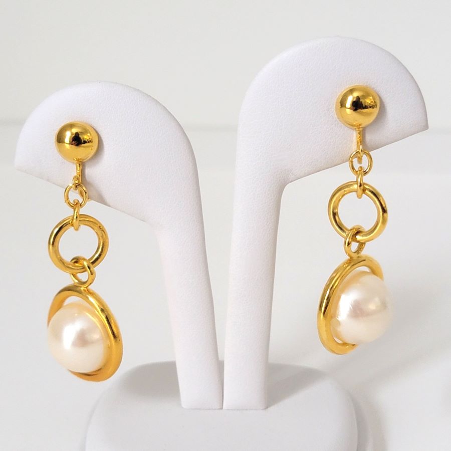 Avon faux pearl drop, clip on earrings, with gold tone rings, shown on a display stand.