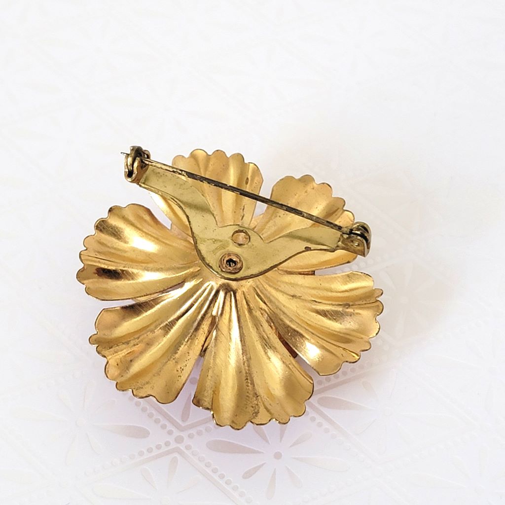 Back view of enamel flower pin, showing its gold tone surface.