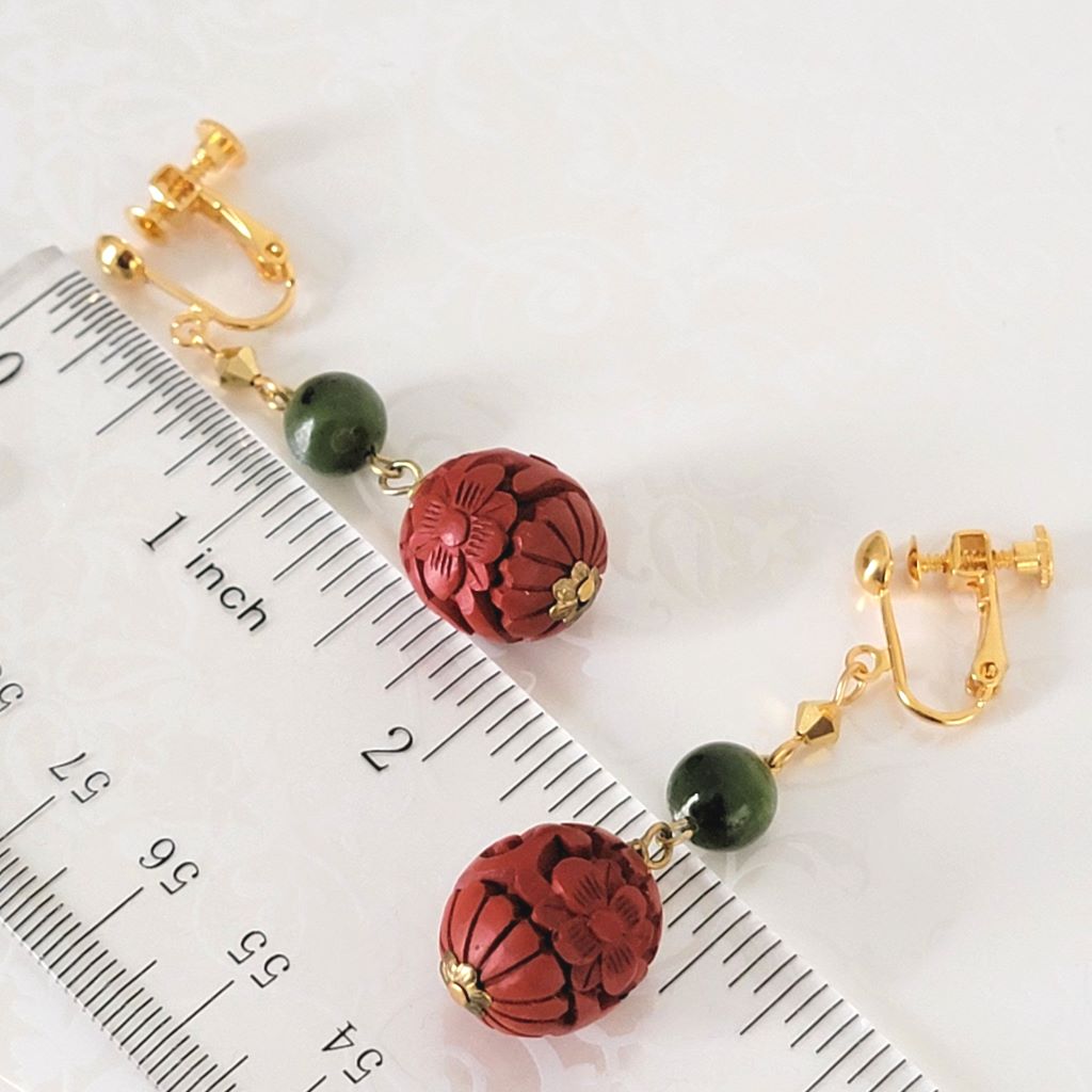 Floral cinnabar-look earrings with green stones, on gold tone clips, shown next to a ruler.
