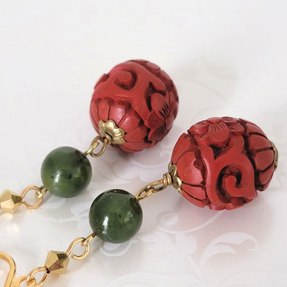Closeup view of cinnabar style red beaded earrings, with green stone accents.