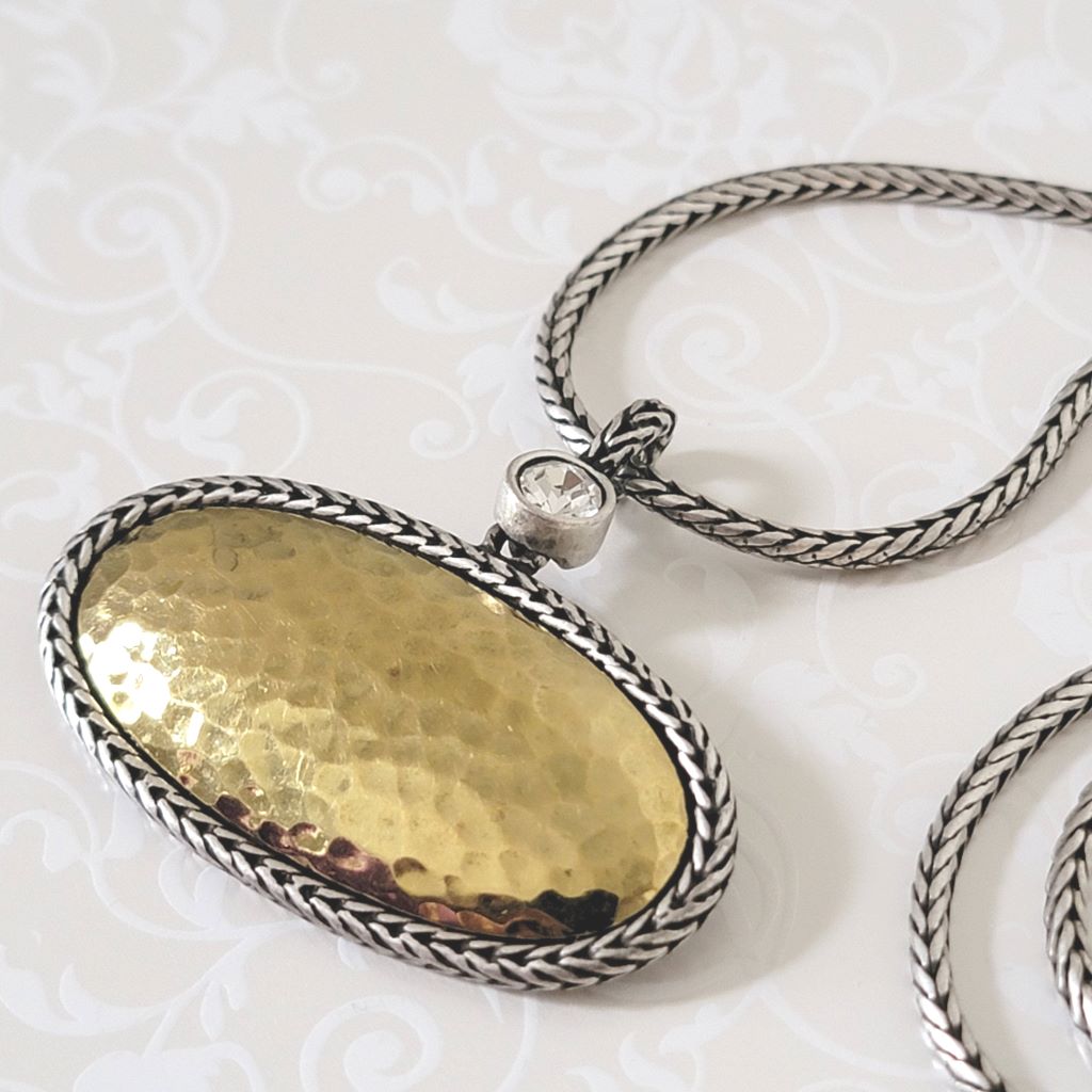 Closeup view of a Premier Designs necklace pendant in hammered gold and silver tone, with foxtail chain and crystal accent.
