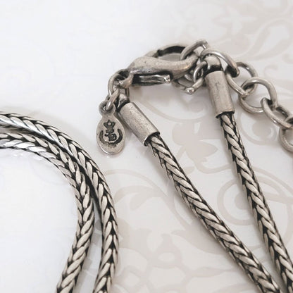 Closeup view of a Premier Designs necklace clasp on a silver tone foxtail chain, showing signature mark logo tag.