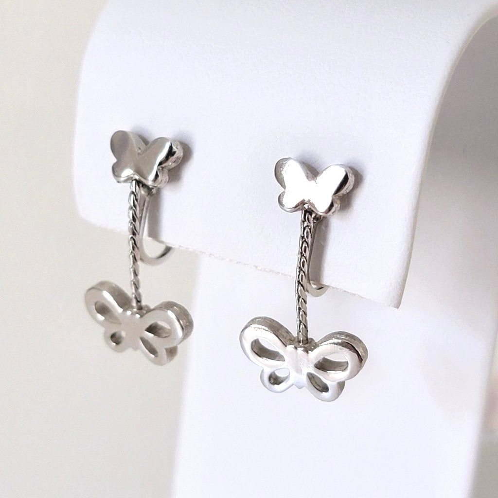 Silver tone Crown Trifari butterfly dangle clip earrings, shown on a display stand.