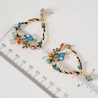 Enamel blue bird teardrop hoop earrings next to a ruler.