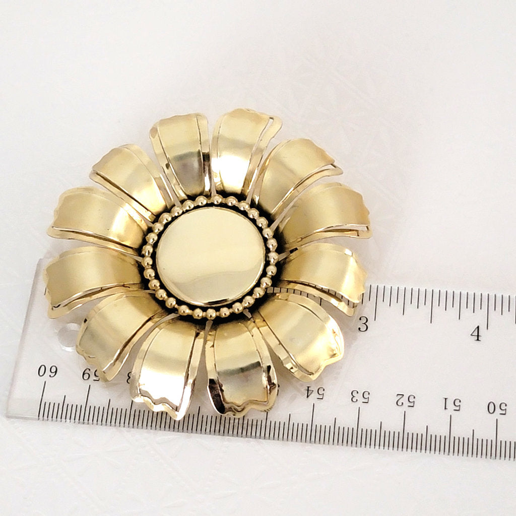 big 60s vintage flower pin, next to a ruler