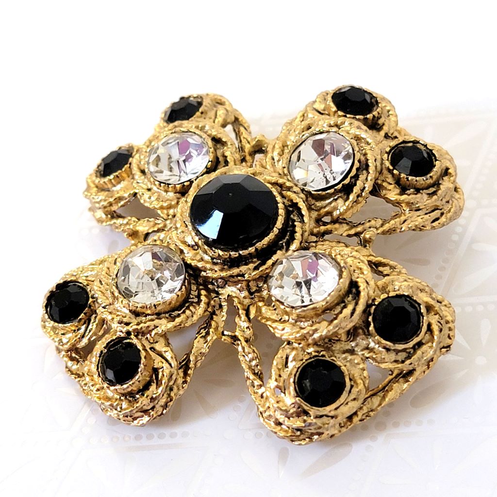 Side view of gold tone Maltese cross brooch, with black and clear rhinestones.