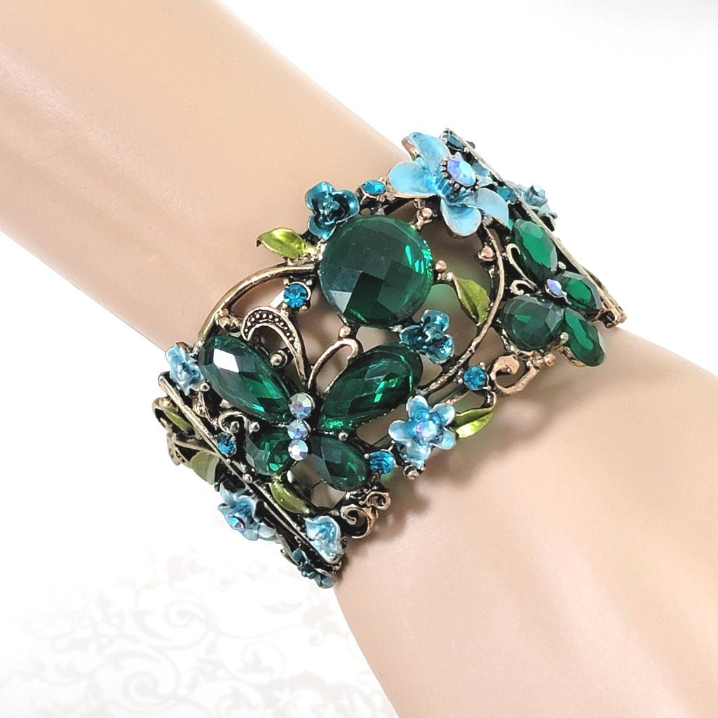 Emerald green rhinestone butterfly cuff bracelet, with blue flower accents. Shown on wrist.