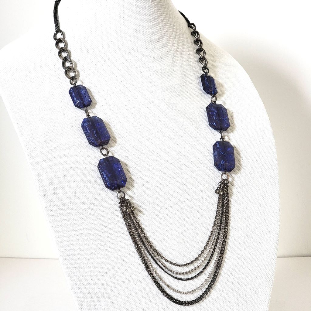 Kenneth Cole long blue beaded and gunmetal chain necklace, with rhinestone accents, shown on a display stand.