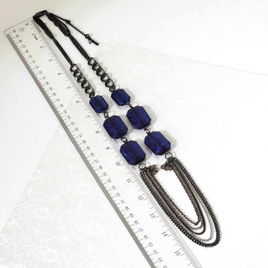 Kenneth Cole long blue bead and gunmetal chains necklace next to a ruler.