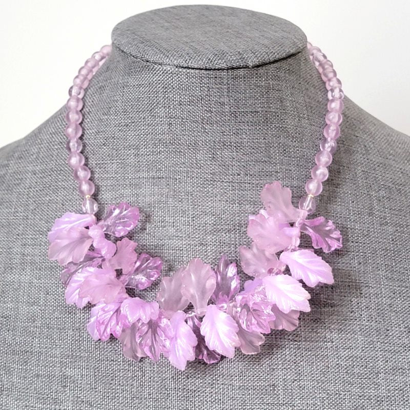 Pastel purple plastic leaves beaded necklace, on a gray display stand.
