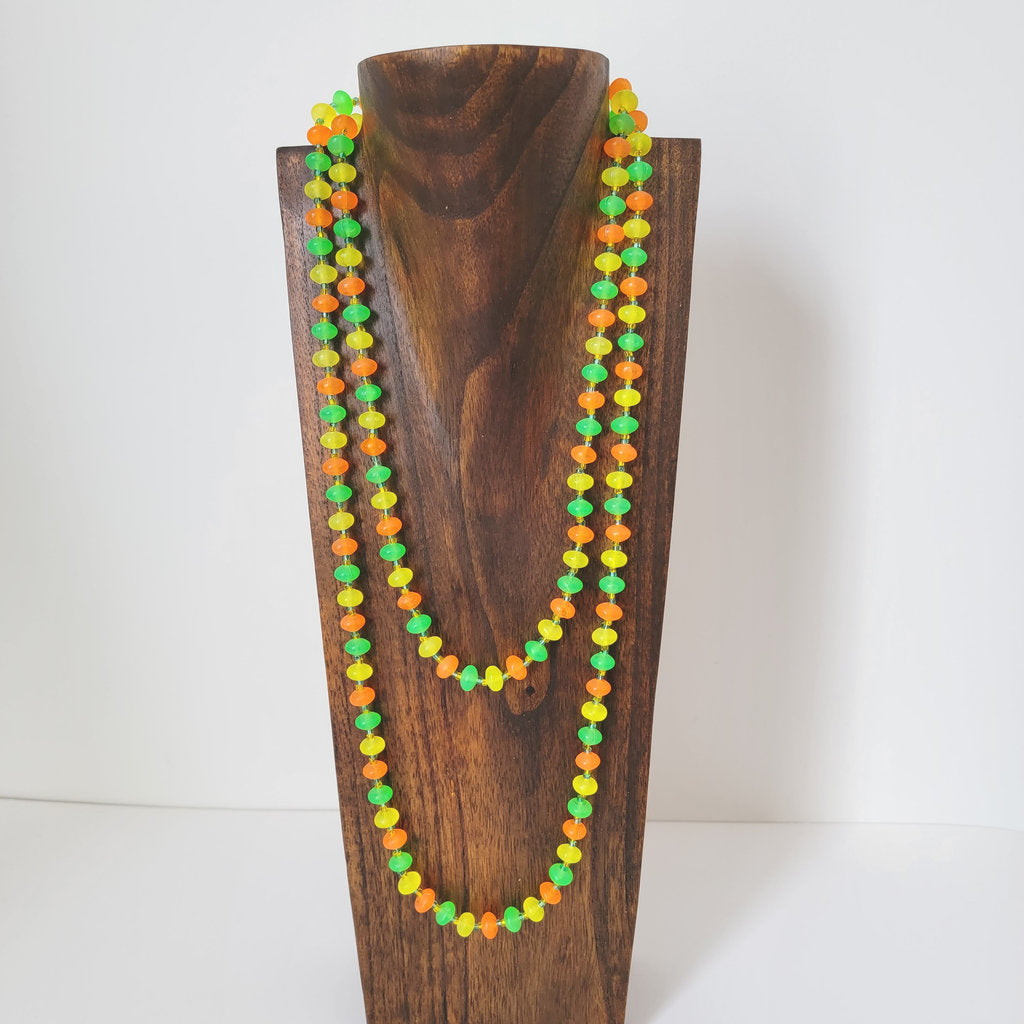 Vintage long 60s necklace, with bright color plastic beads, on a display stand.