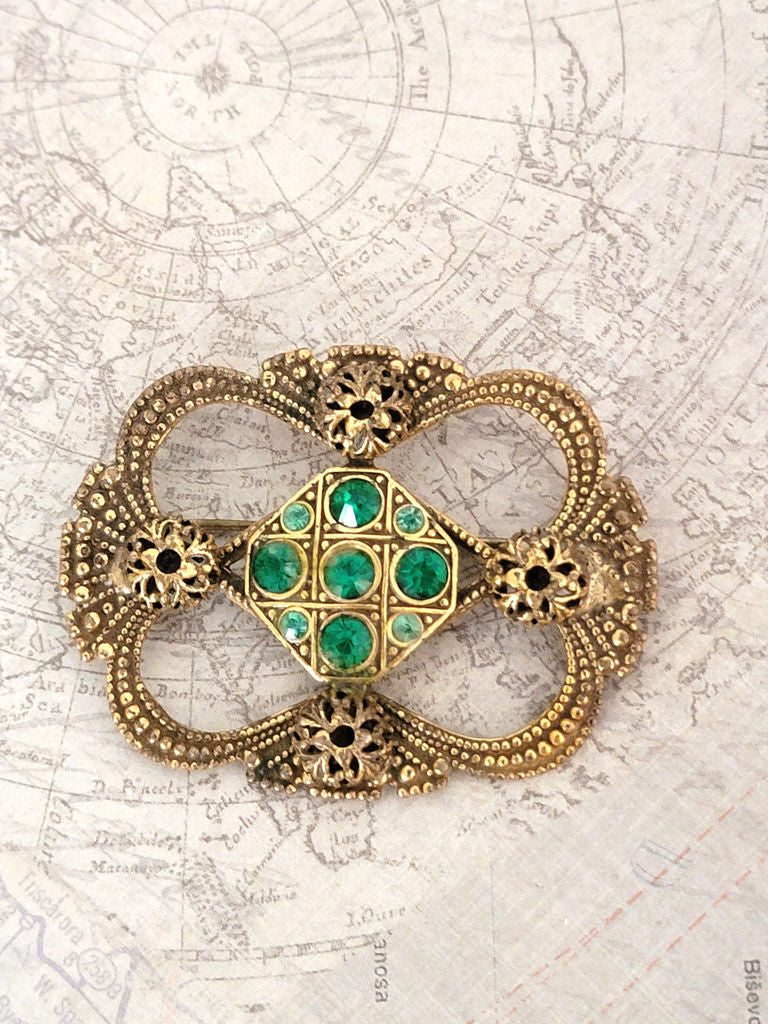 old world style brooch, brass tone open setting, with green rhinestones, and filigree accents