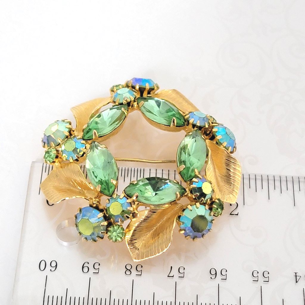 Light spring green rhinestone brooch, with gold tone leaves, shown next to a ruler.