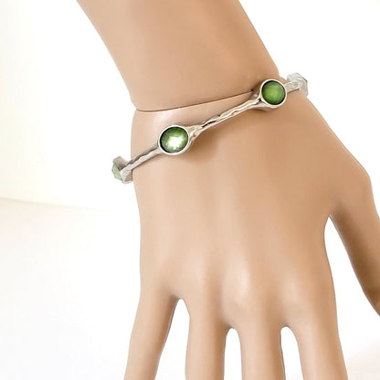 Premier Designs skinny silver tone bangle bracelet, with faceted green acrylic accents. Shown on a wrist