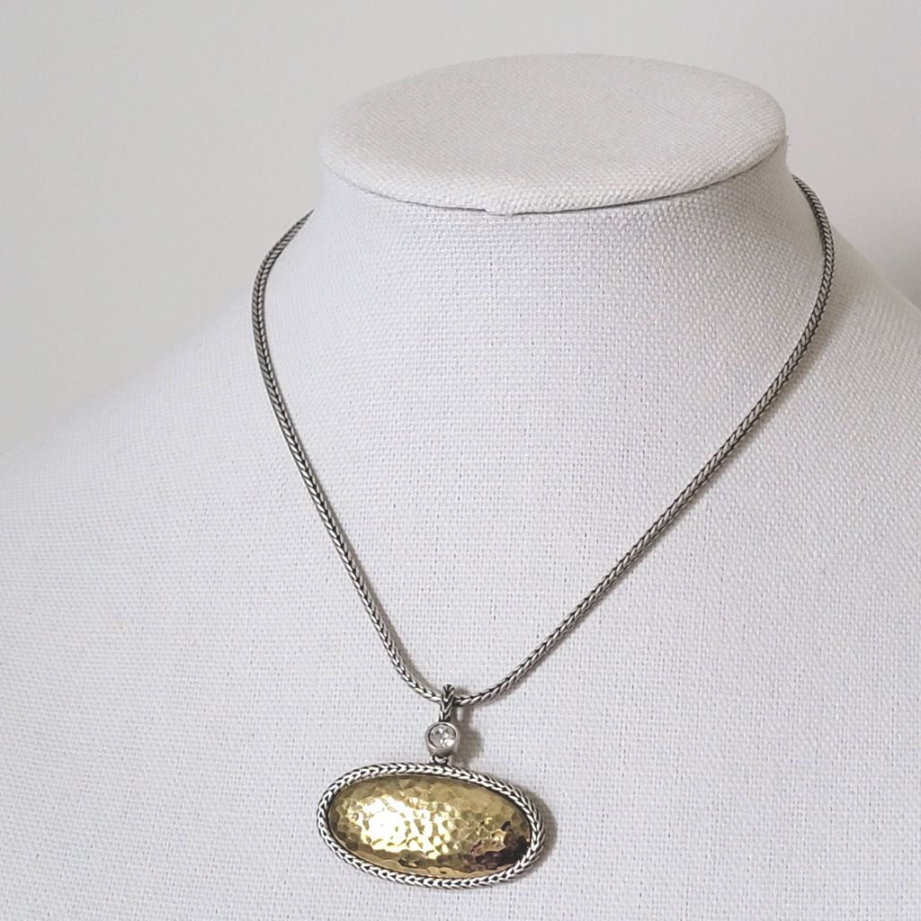Premier Designs oval pendant choker in hammered gold and silver tone, with foxtail chain and crystal accent. Shown on a display stand.