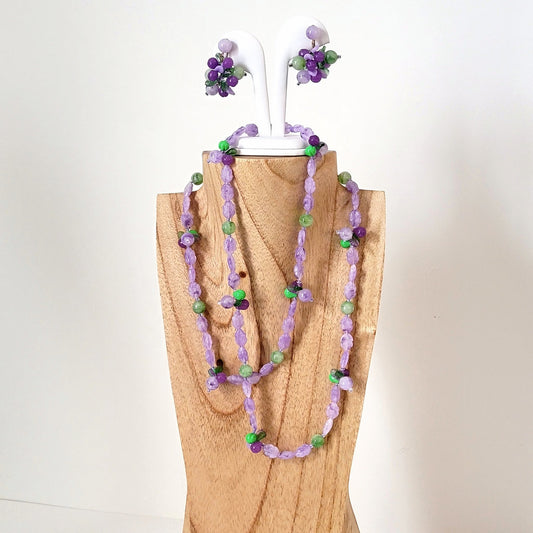 Vintage purple and green lucite plastic, beaded necklace and clip on earrings set. Green leaves accent the jewelry, made in Germany. Set is on a display stand.
