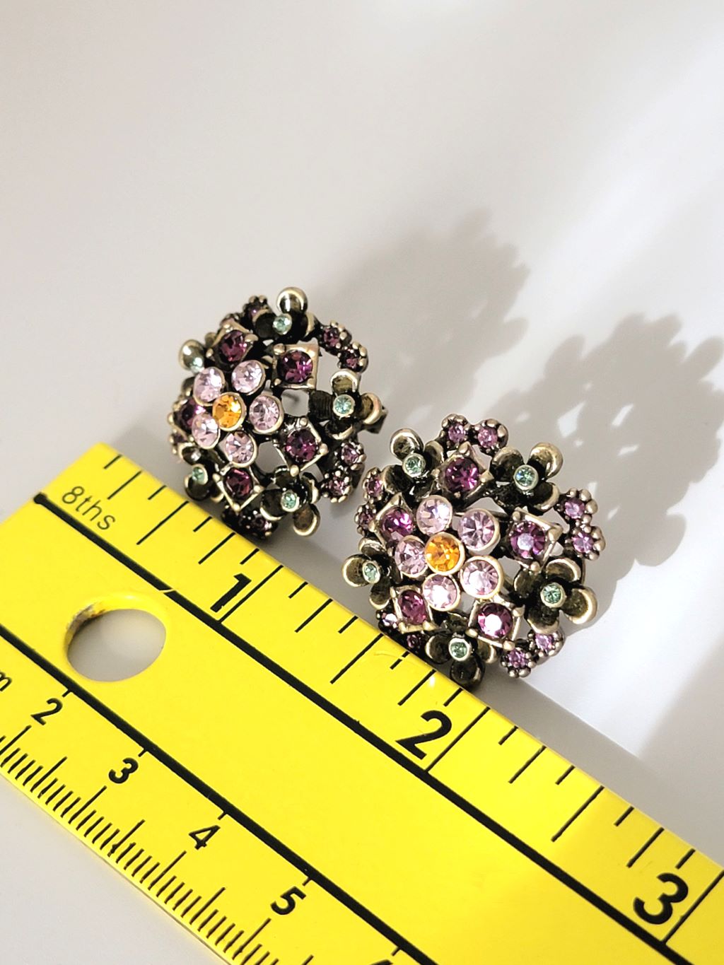 Rhinestone post earrings, in floral settings, with jewel tone crystals, next to a ruler.