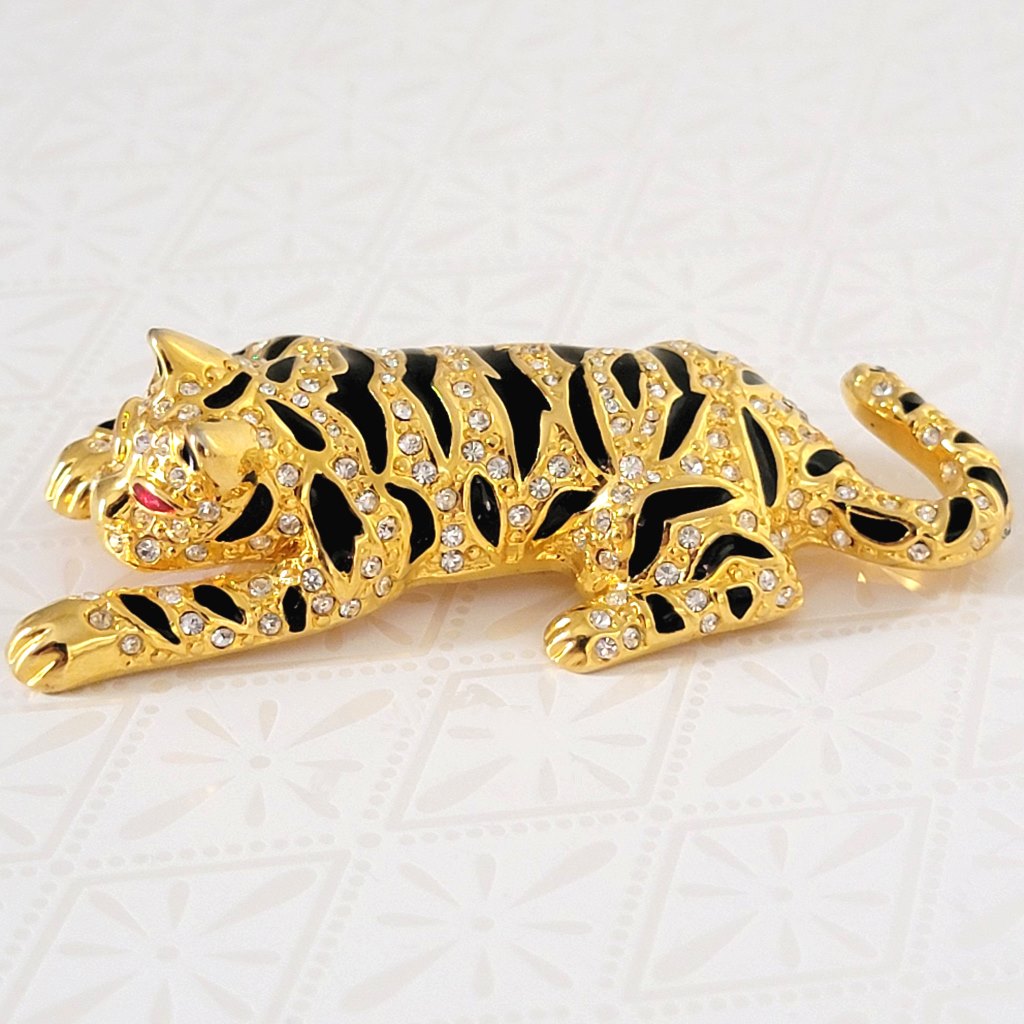 Reclining tiger brooch, gold tone, with crystals, black stripes and red eyes.