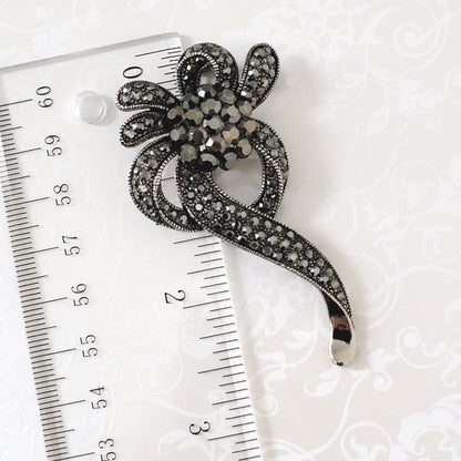 Silver glass rhinestone flower ribbon style brooch, shown next to a ruler.