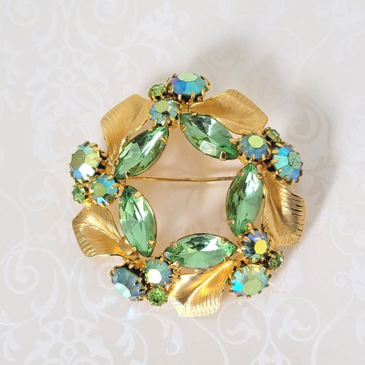 Light spring green rhinestone brooch, with gold tone leaves, in a circle, wreath-like design.