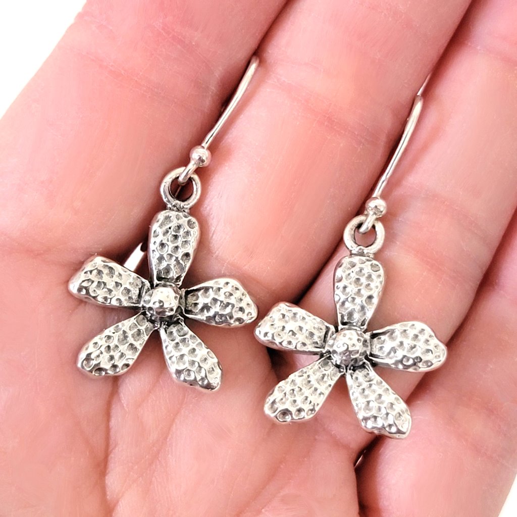 Sterling silver textured flower dangle earrings, shown in hand.