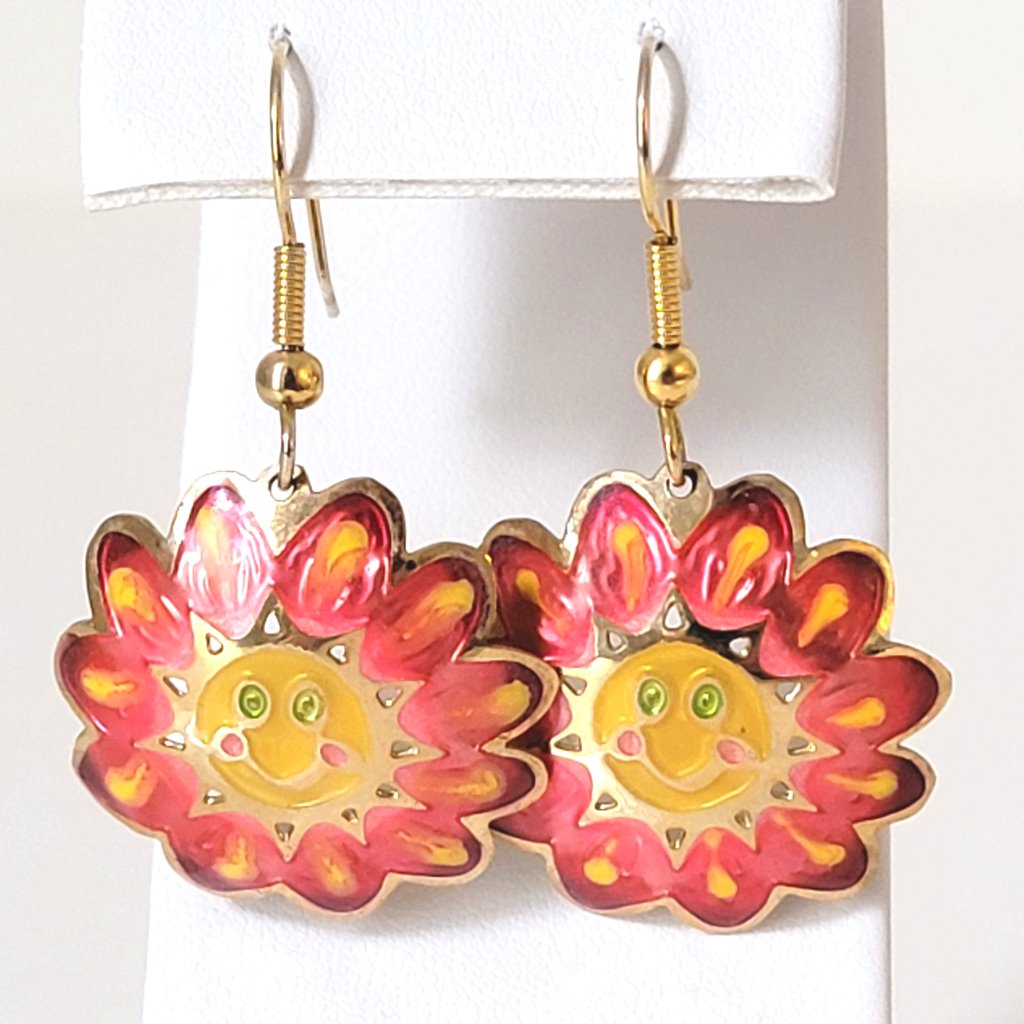 Vintage Two Hands brand pink and yellow enamel flower dangle earrings, with smiley faces and green eyes. Shown hanging on a display stand.