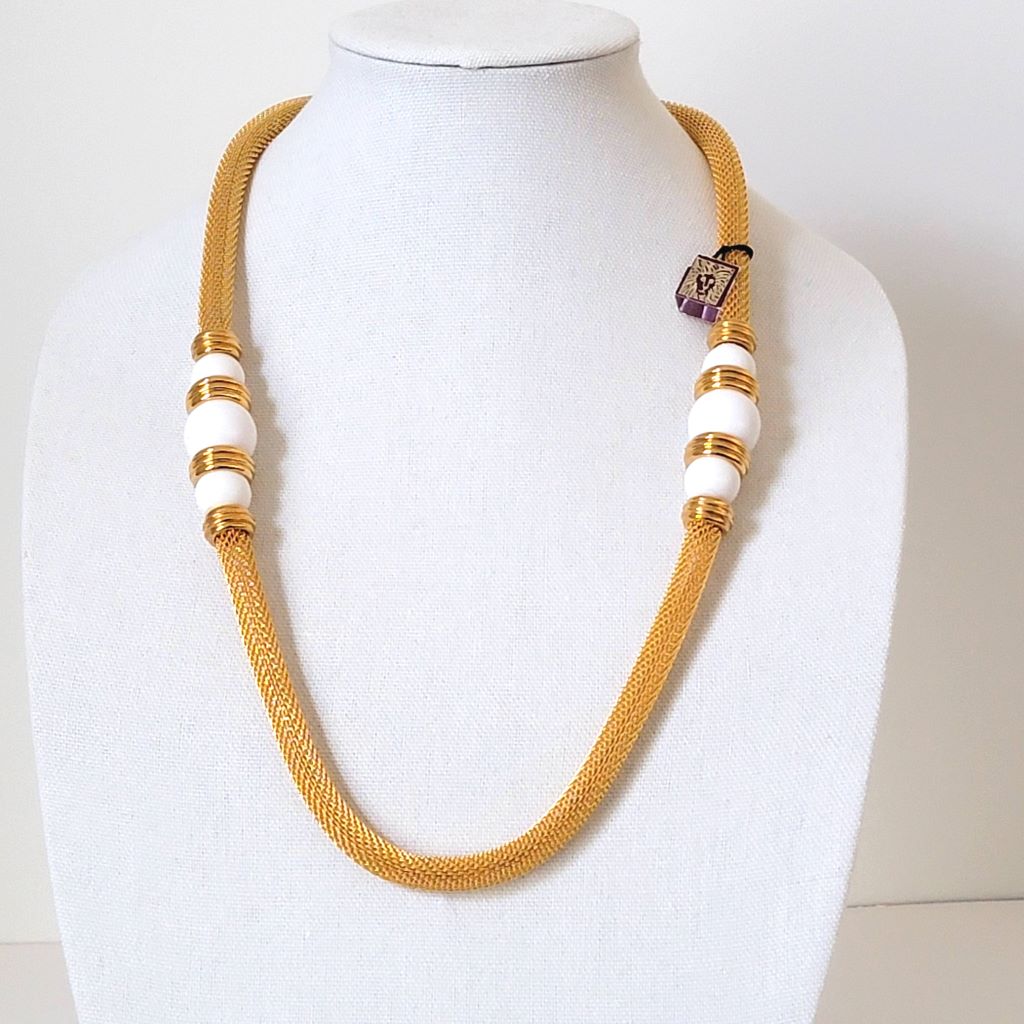 Vintage Anne Klein gold tone mesh tube style necklace, with large white bead accents. Shown on a white display stand.