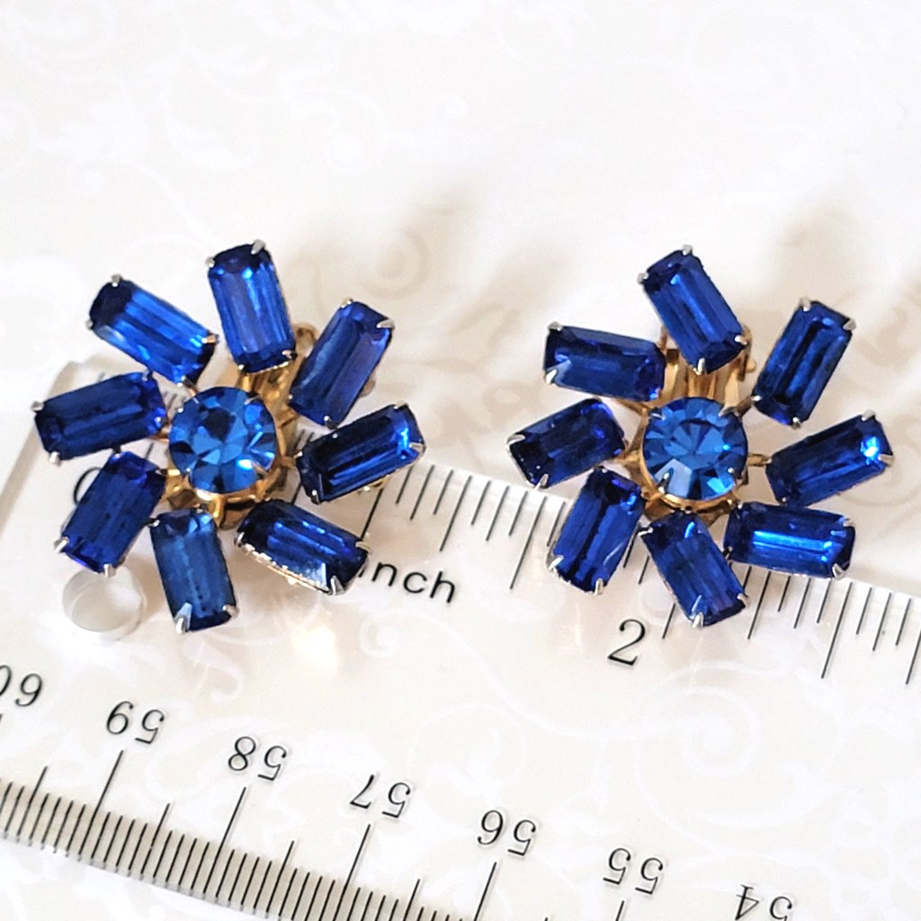 Vintage sapphire blue, baguette rhinestone clip on earrings, with a pinwheel style prong setting. Shown next to a ruler.