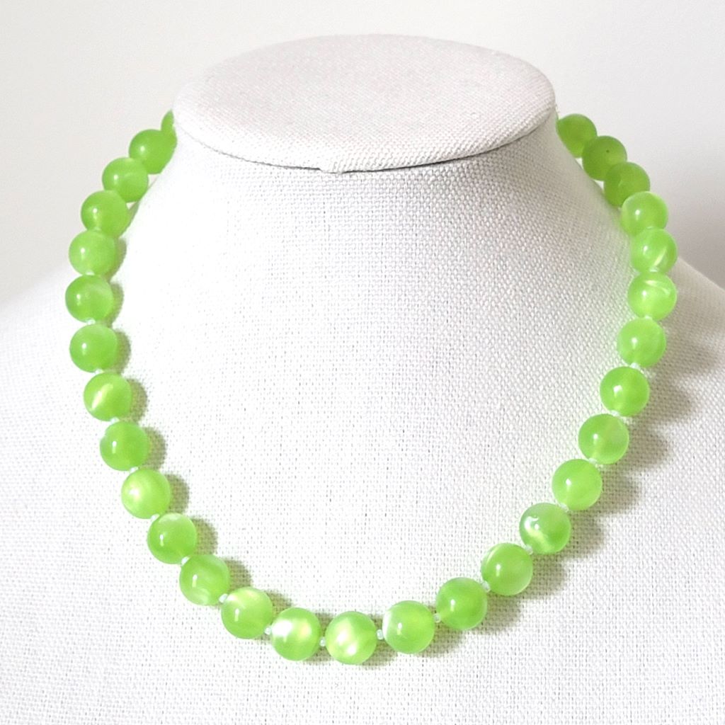 Vintage bright green plastic beaded moonglow necklace, on a display stand.