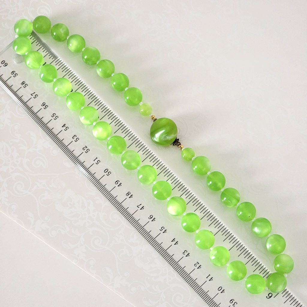 Vintage bright green beaded moonglow necklace,next to a ruler.