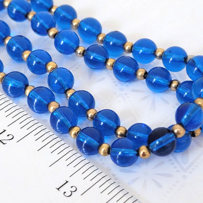 Vintage translucent blue plastic beaded, long 60s necklace, shown closeup, next to a ruler.