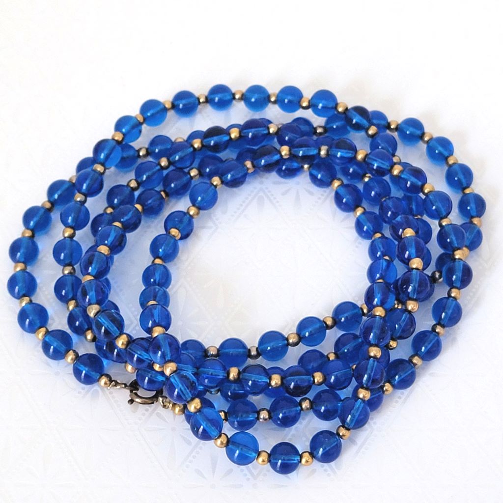 Vintage translucent blue plastic beaded, long 60s necklace, coiled on table.